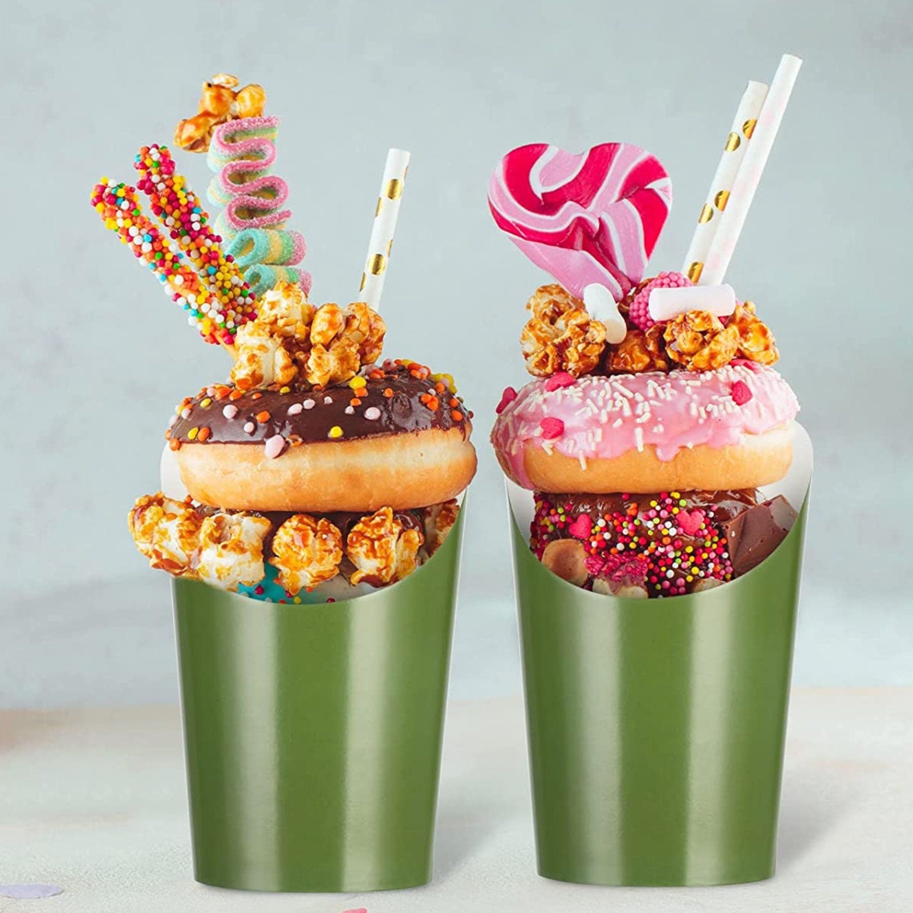 Two green charcuterie cups filled with donuts, popcorn, and candy for dessert display.