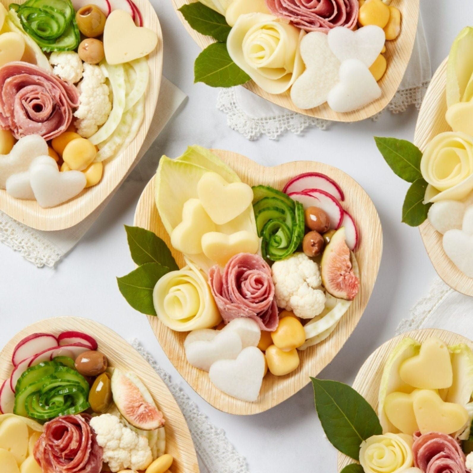 Heart-shaped bamboo charcuterie plate with cheeses, meats, and pink heart toothpick