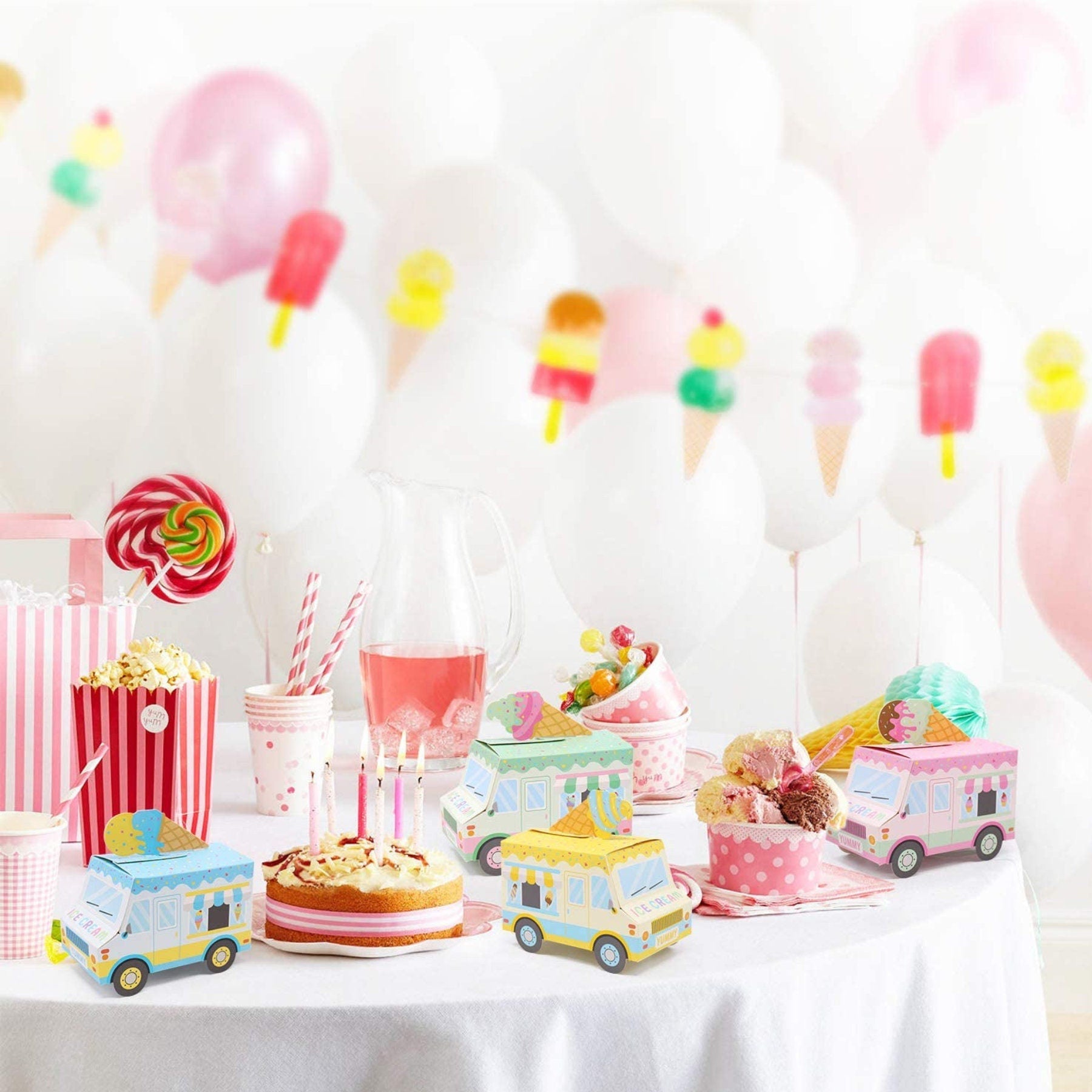 Ice cream truck favor boxes arranged on a pink party table with balloons and desserts.