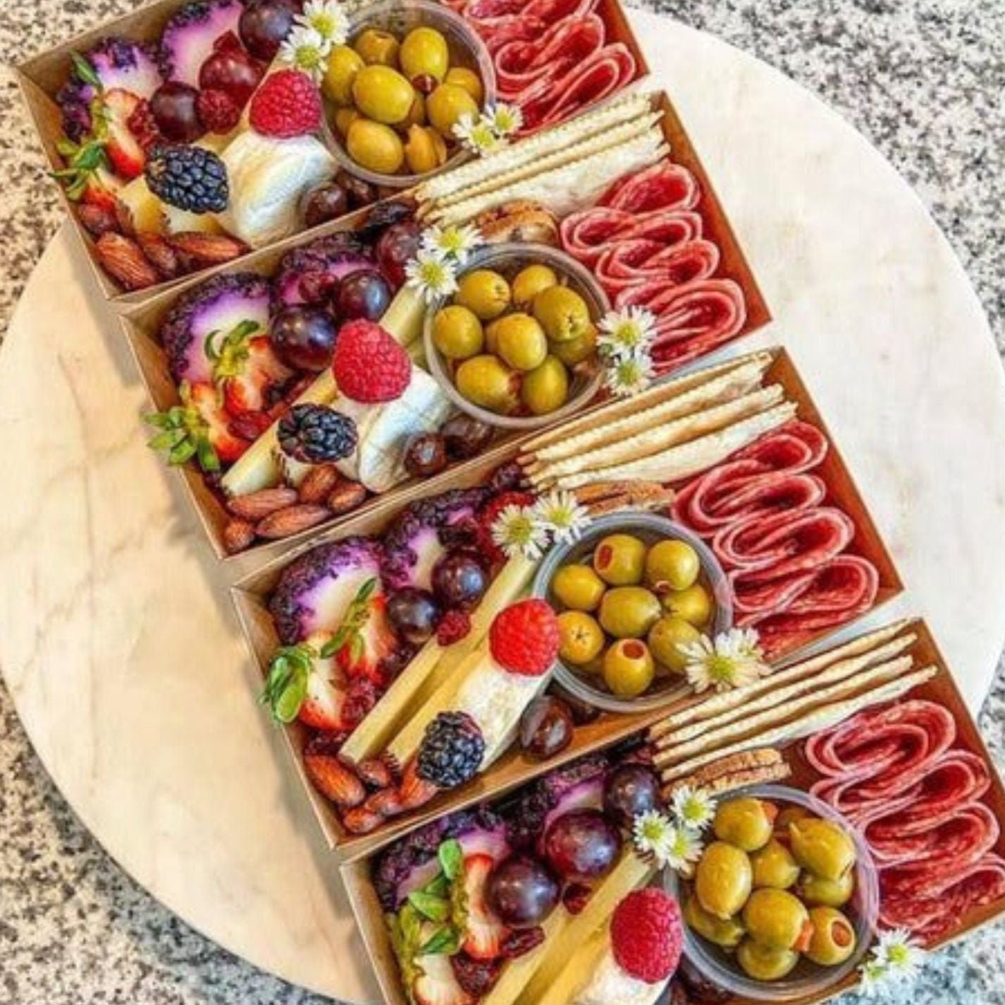 Multiple disposable charcuterie boxes filled with olives, cheese, meats, and fruit.