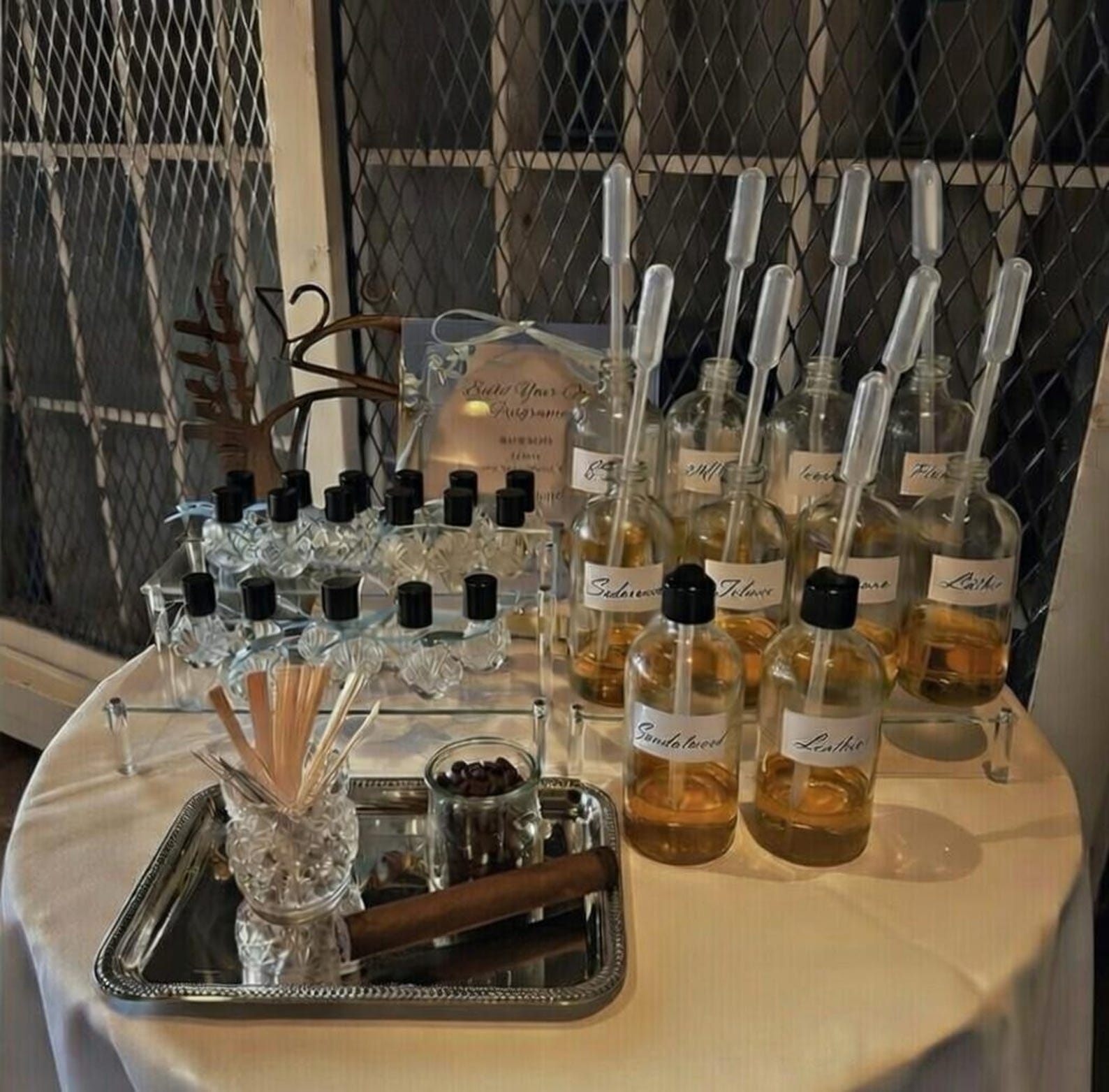 Lifestyle display of a men’s DIY cologne making kit set up on a round event table, featuring glass fragrance bottles filled with oils, pipettes, scent strips, and mixing tools—ideal for bachelor parties, groomsmen proposal gifts, and interactive fragrance bars.