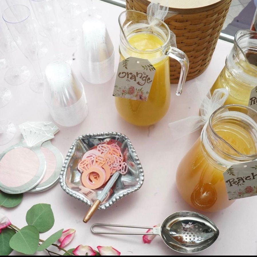 Styled brunch mimosa bar table with juice carafes, fruit garnishes, and signage