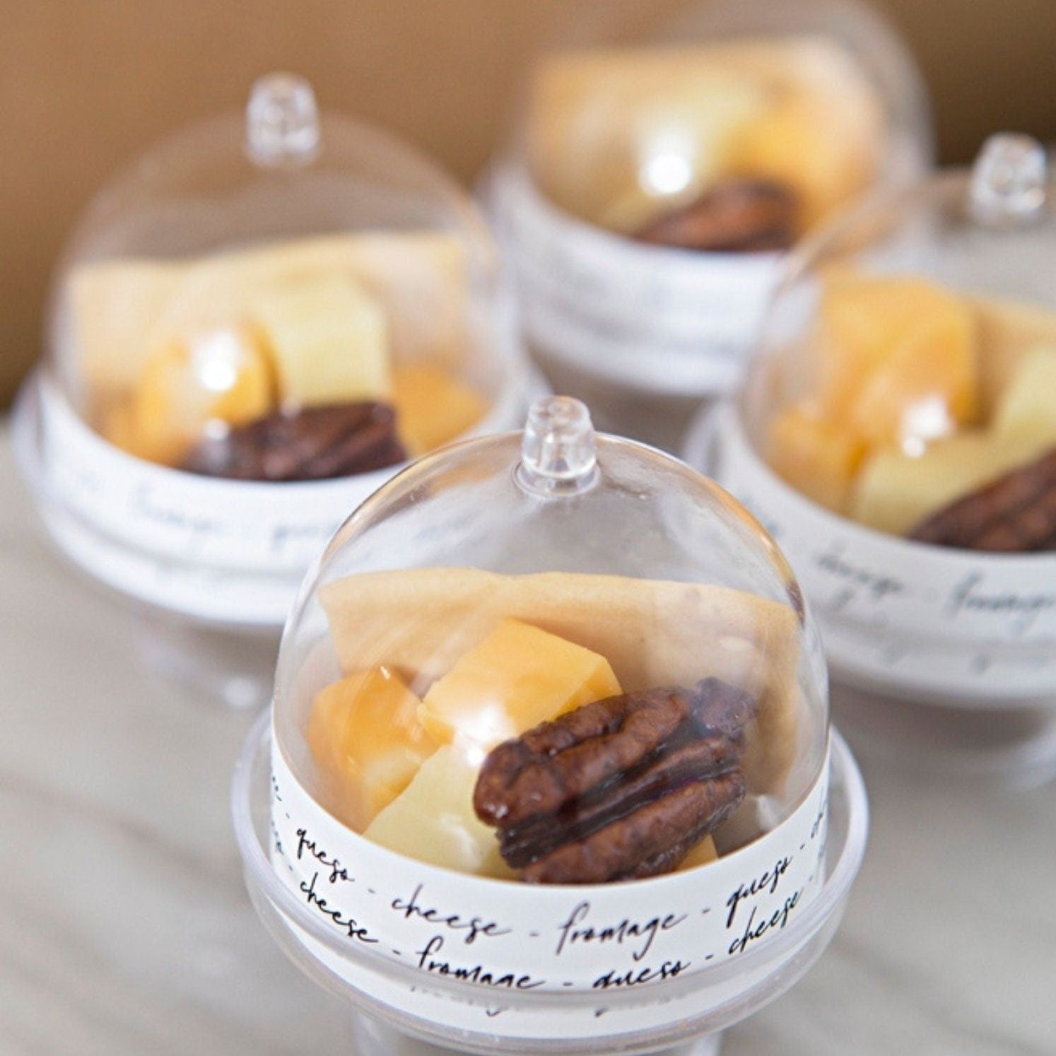 Set of mini cake stands filled with cheese cubes and snacks under dome lids