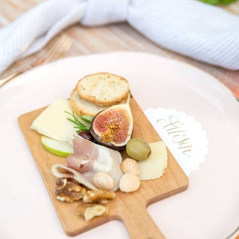 Mini wooden charcuterie board on a plate with fig, cheese, nuts, and crackers at a place setting