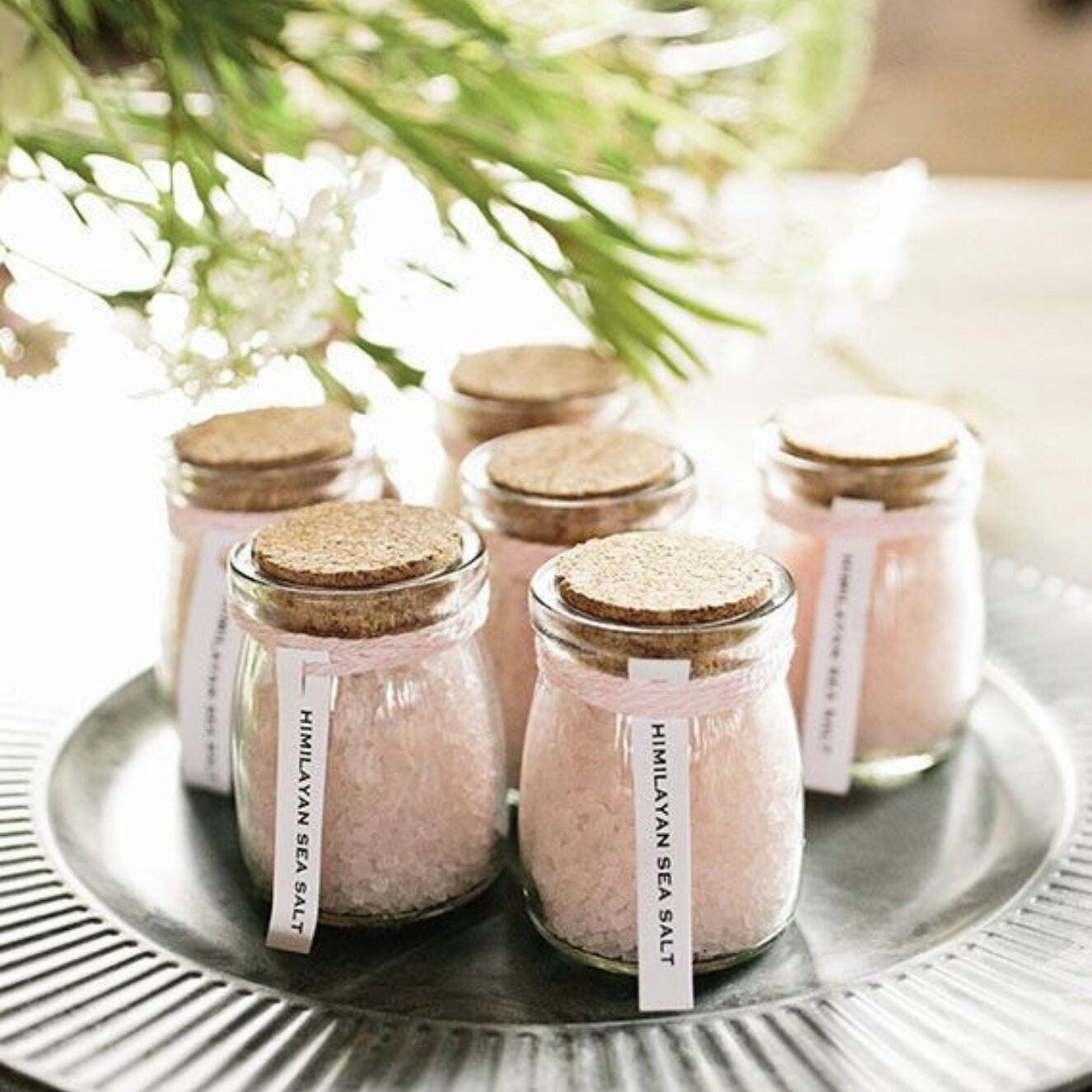 Tray of mini glass jars with cork lids filled with pink Himalayan salt and labeled tags