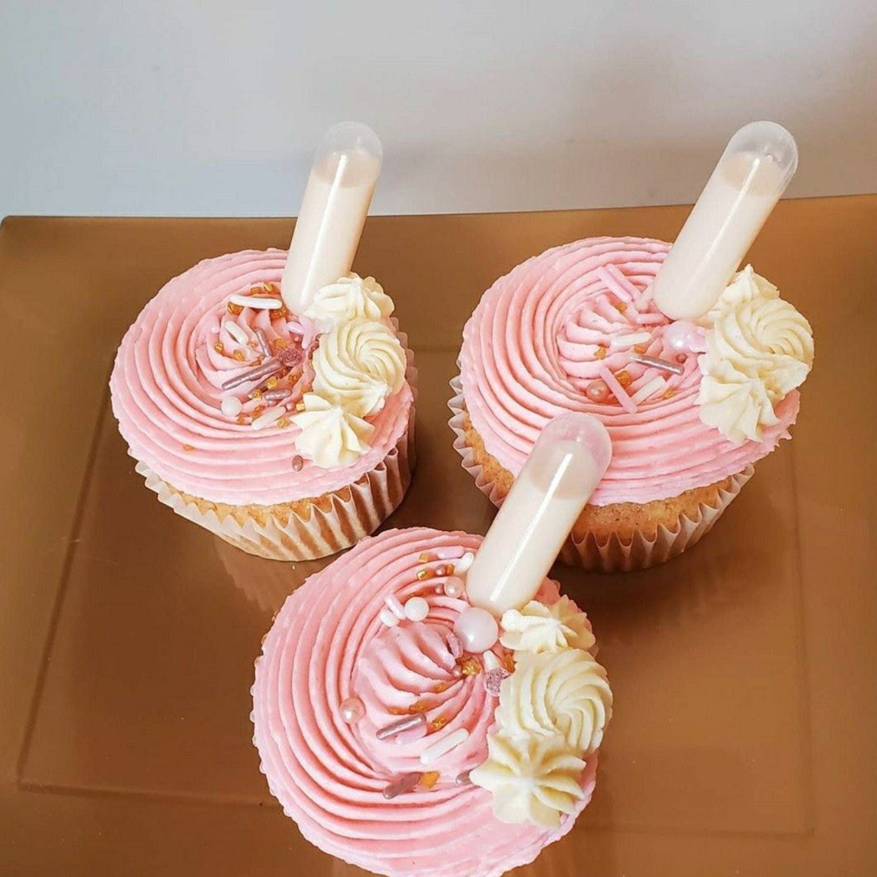 Pink frosted cupcakes topped with mini pipettes for injectable cupcakes