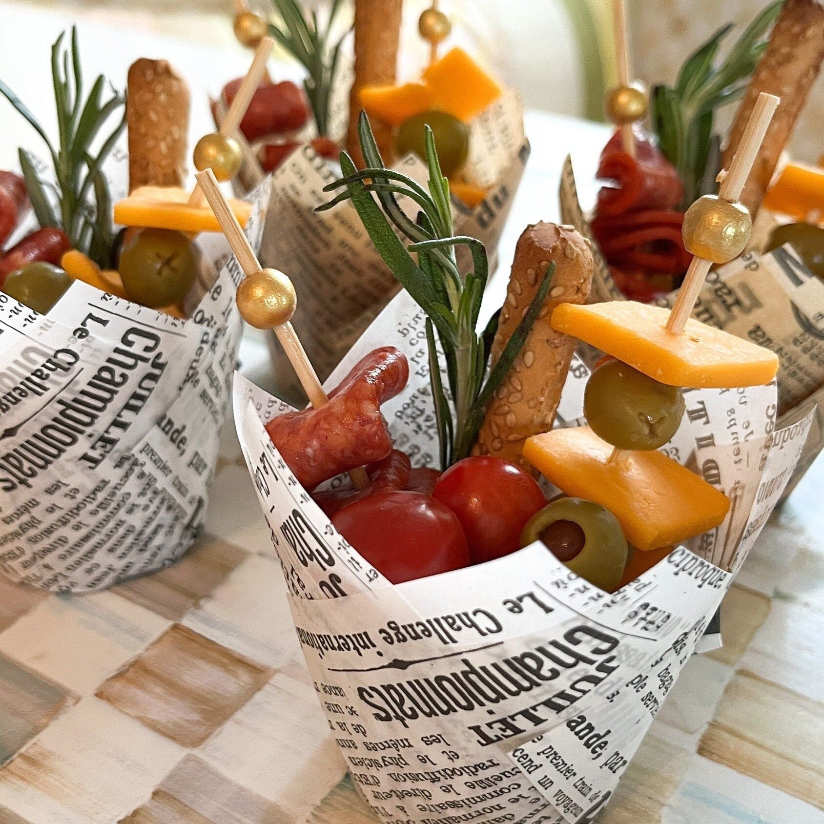 Vintage newspaper print charcuterie cups filled with appetizers and fancy toothpicks on elegant party table