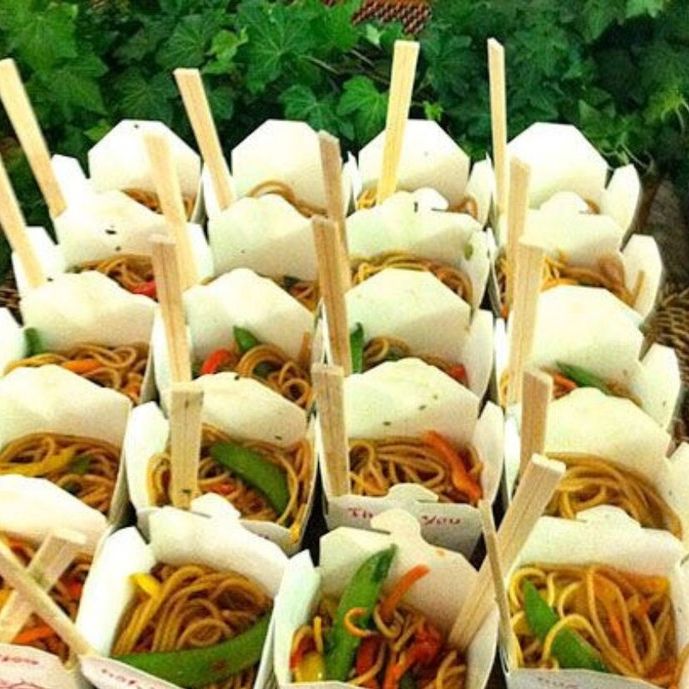 Display of Chinese takeaway containers filled with noodles and chopsticks at outdoor event.