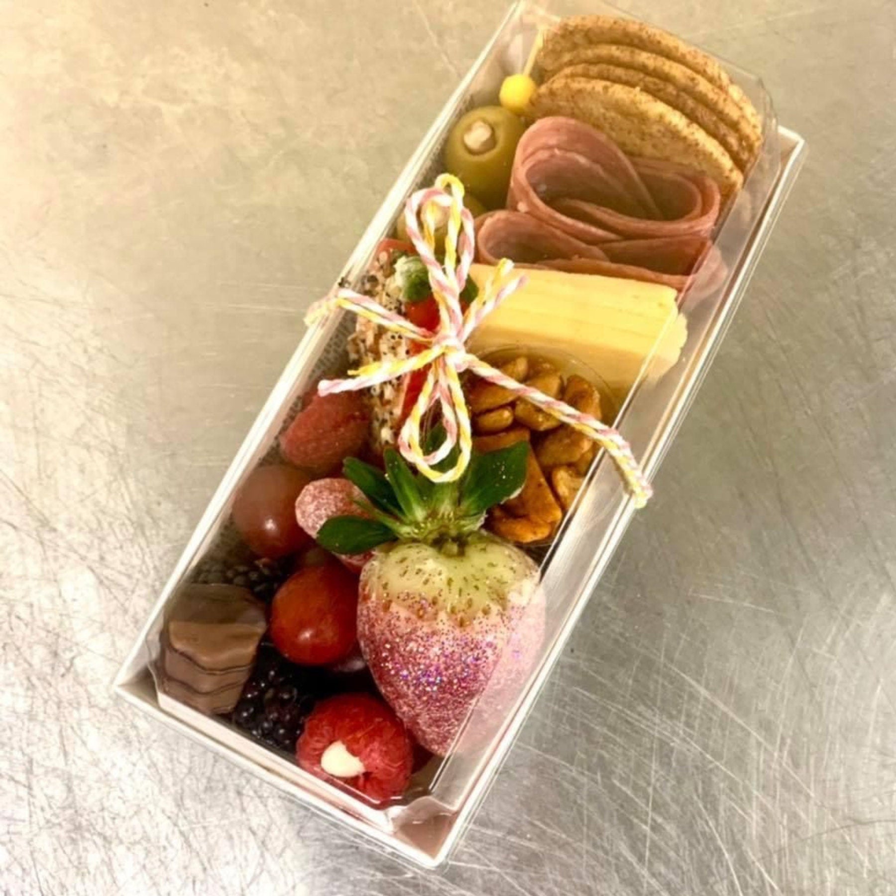 Mini grazing box with fruits, cheese, meats, and cookies tied with string.