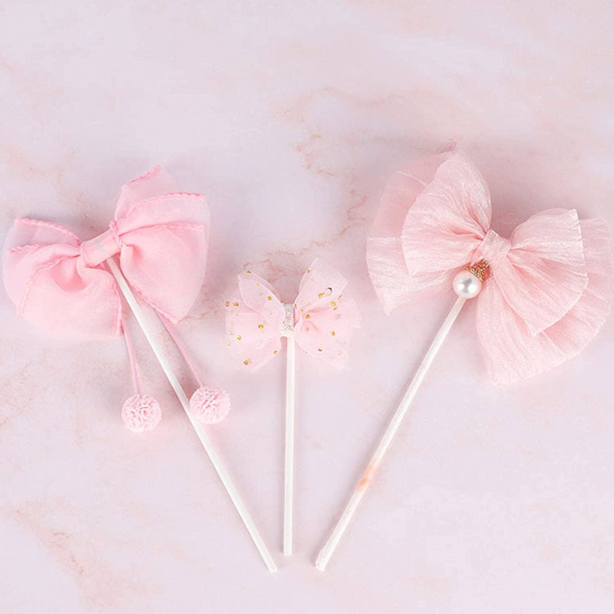 Trio of pink bow cake toppers with tulle, pearl and pom-pom details on marble backdrop