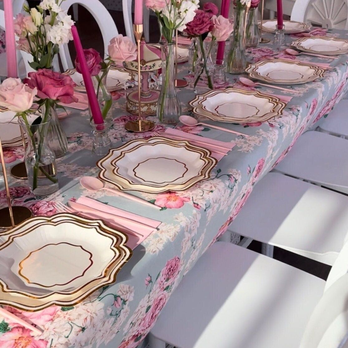 Long floral tablescape set with pink and gold scalloped plates, pink napkins, cups, and cutlery
