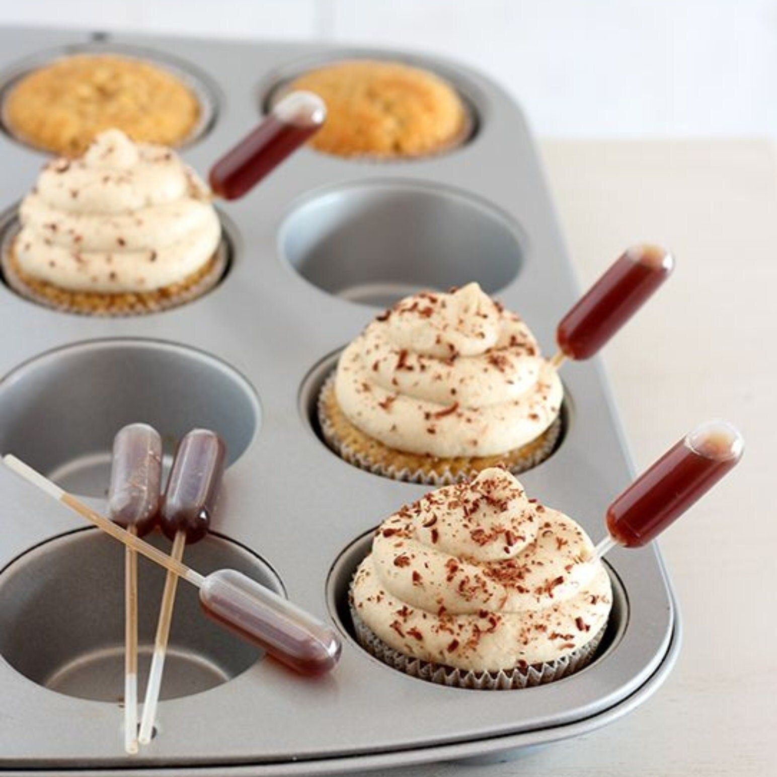 Muffin tin with cupcakes and filled mini pipettes ready for baking decor
