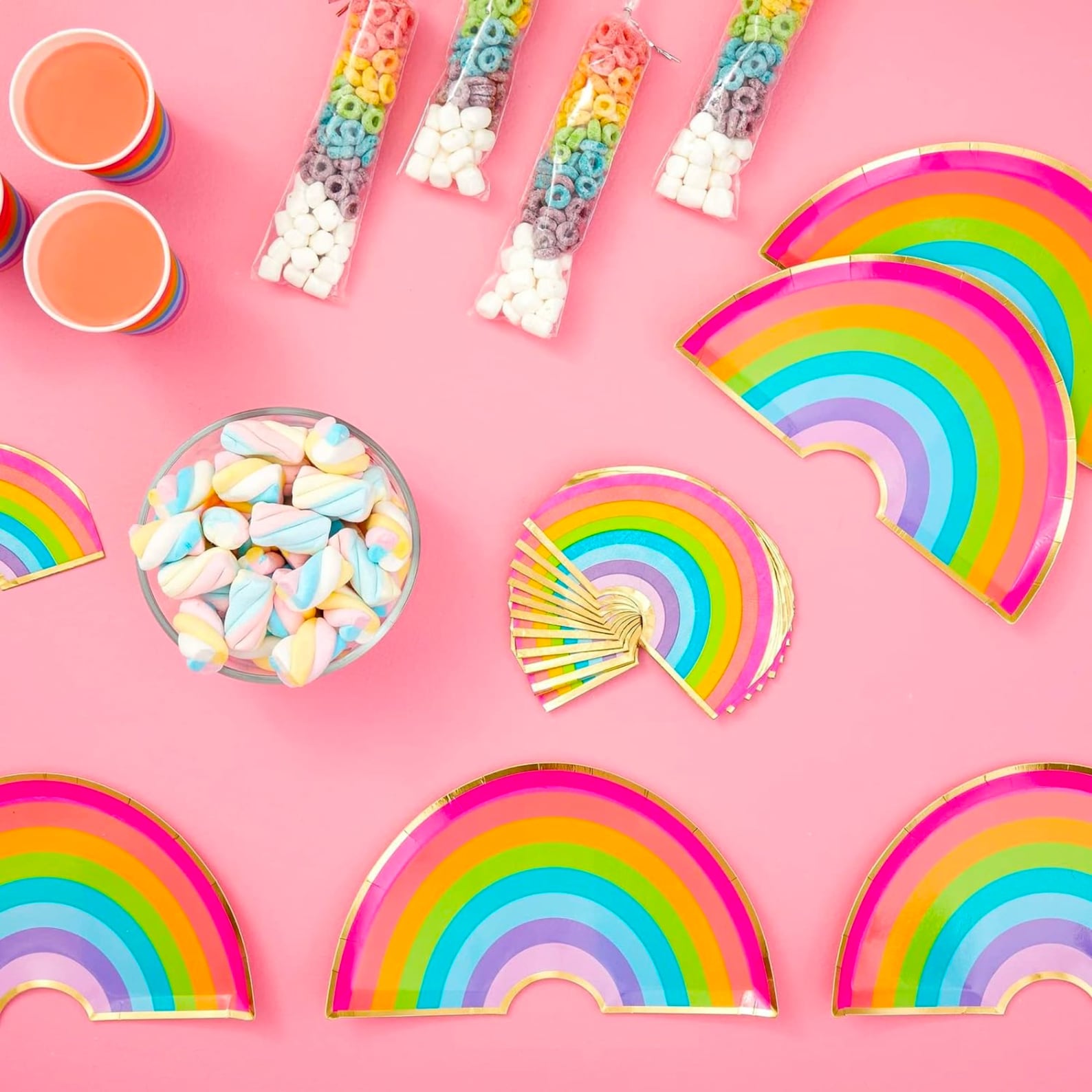 Rainbow plates, cups, and napkins set displayed on pink table with candy and drinks