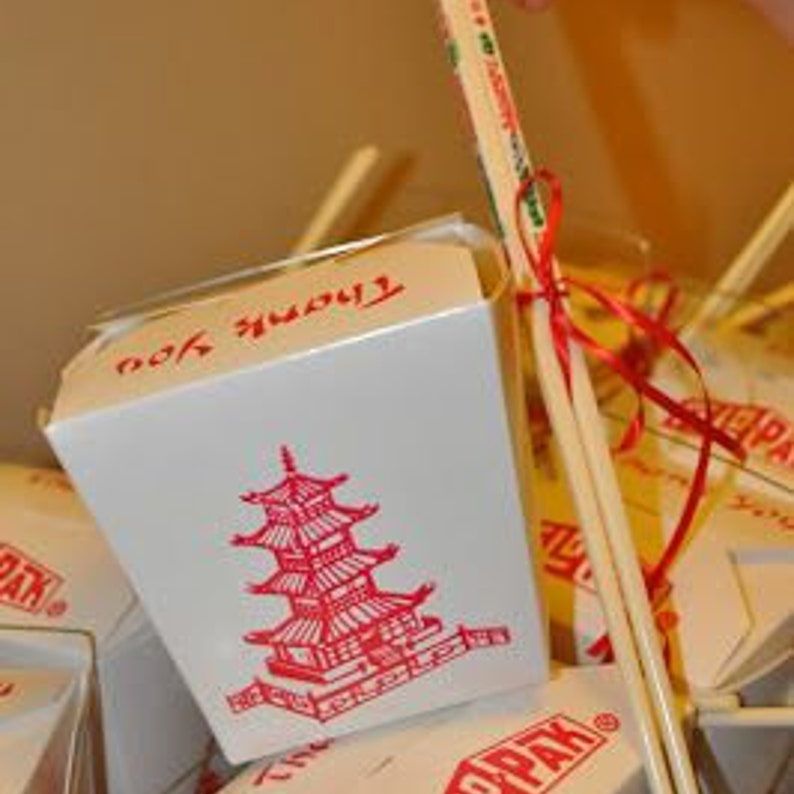 Close-up of single Chinese take out box with red pagoda print and wooden chopsticks tied with ribbon.