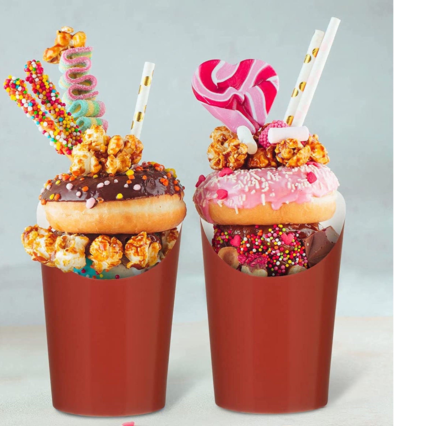 Two red charcuterie cups filled with donuts, popcorn, and candy for a dessert display.