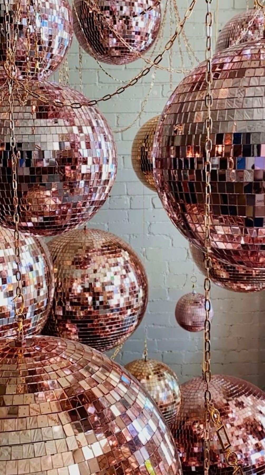 Rose gold disco balls hanging against a light blue wall.