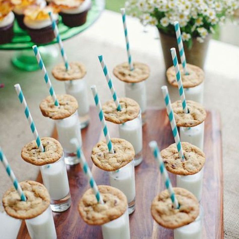 Board of mini dessert cups filled with milk and topped with cookies and blue straws