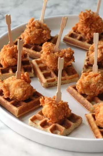 Waffles topped with fried chicken bites on a white plate.