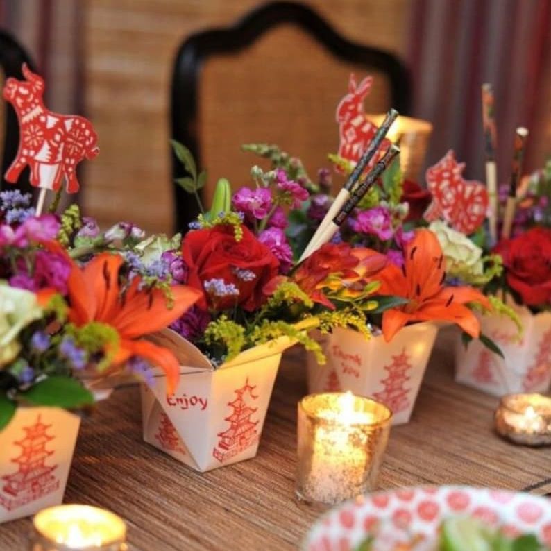 Colorful wedding catering display with Chinese food boxes and chopsticks surrounded by flowers.