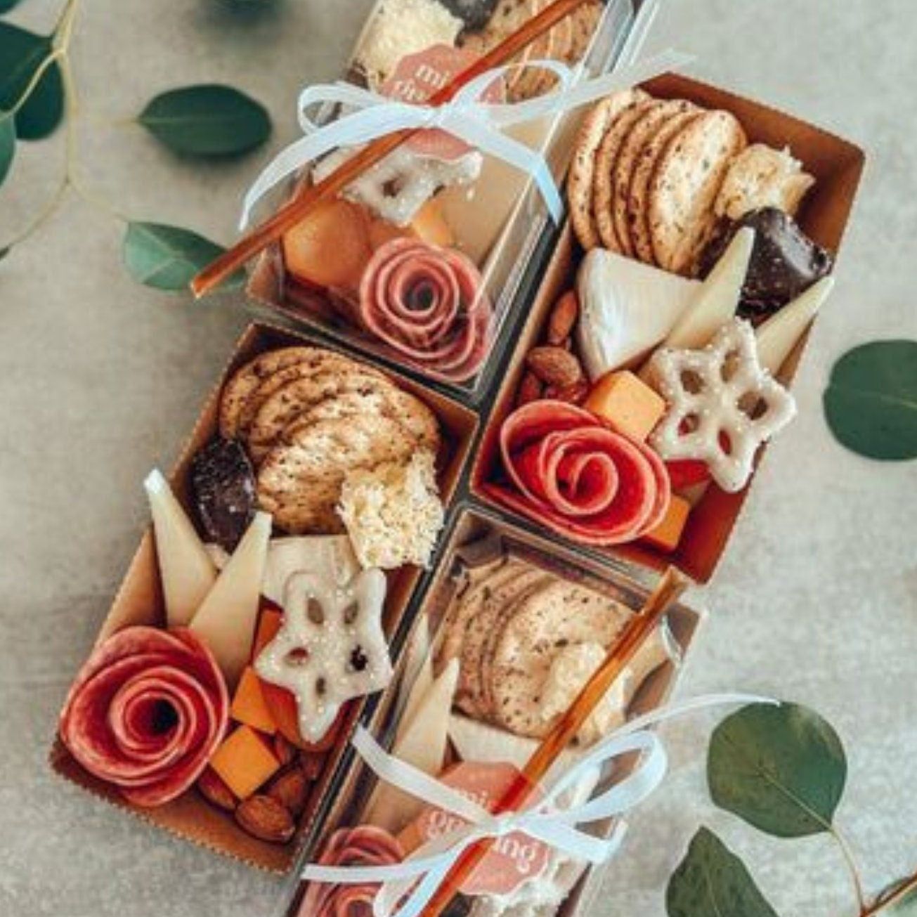 Small charcuterie boxes filled with meats, cheeses, crackers, and tied with ribbon.