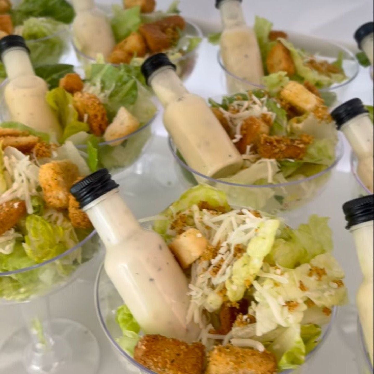 Clear acrylic salad cups with 4oz or 8oz options, mini dressing bottles, and forks on an elegant table setting for a party.