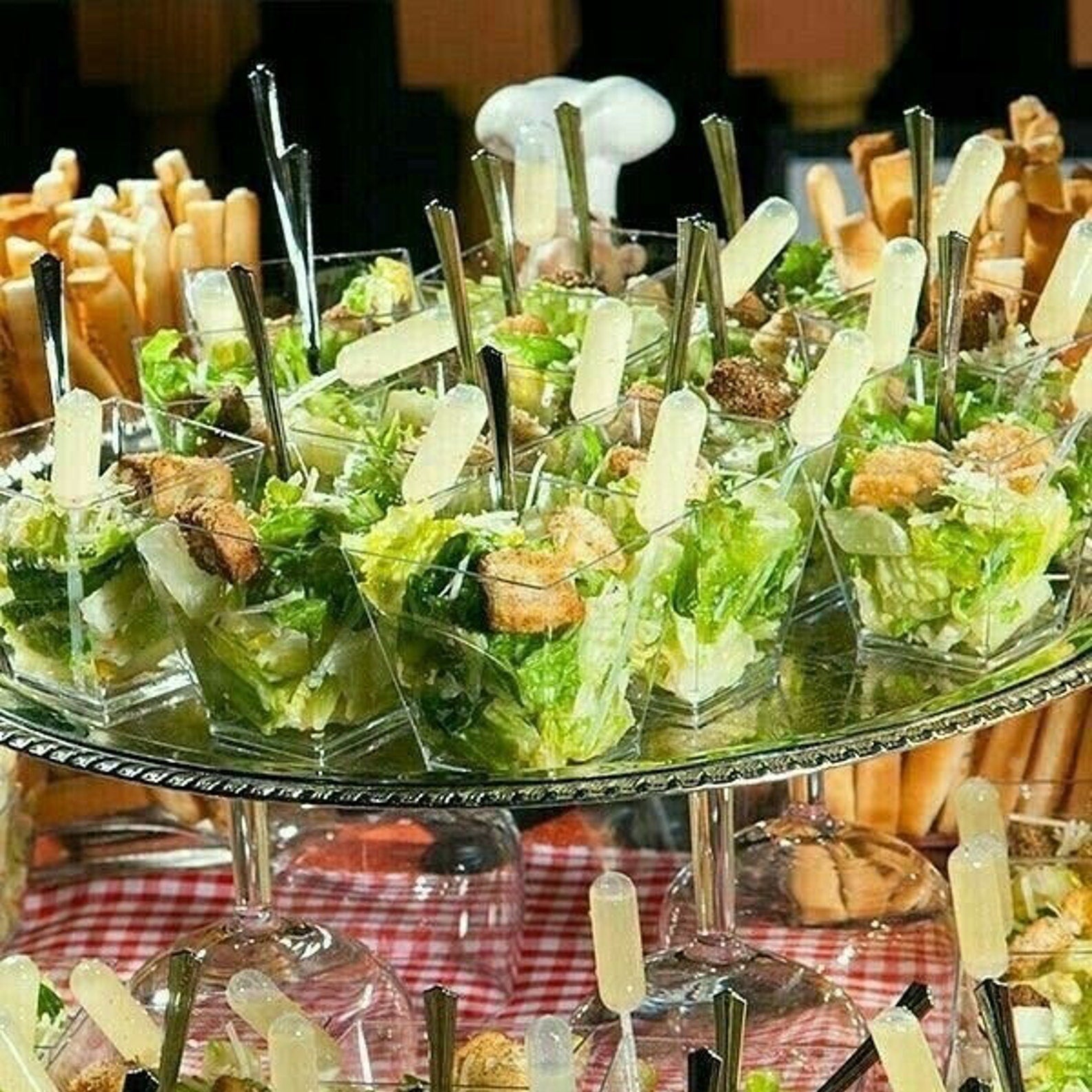 Clear acrylic salad cups with mini dressing pipettes, and forks on an elegant table setting for a party.