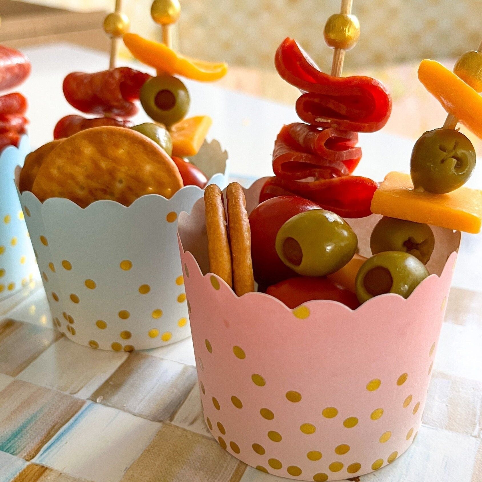 Close-up of disposable charcuterie cups filled with snacks and elegant gold toothpicks for weddings and grazing tables.