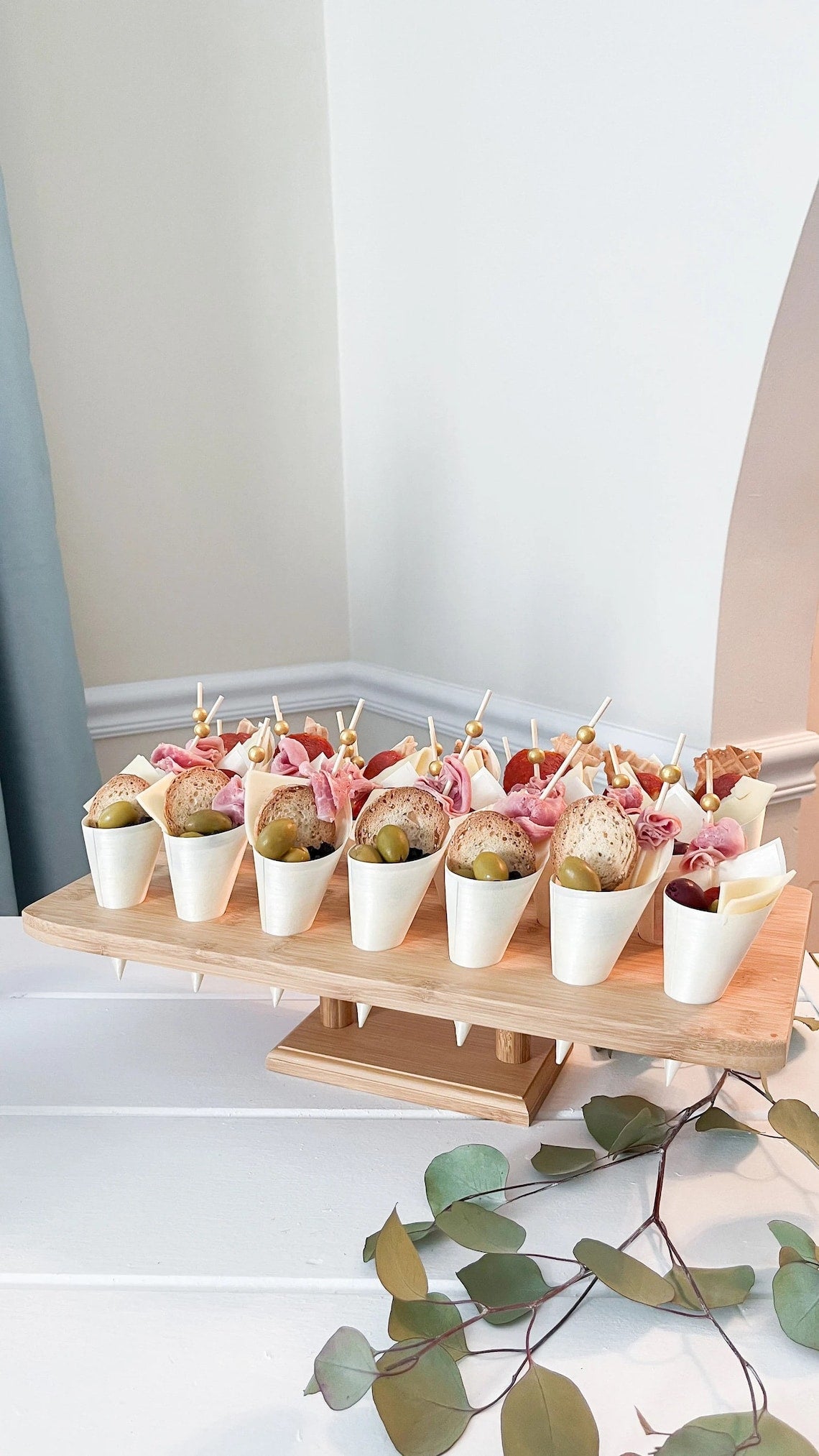 Mini charcuterie cones with gold beaded skewers. Disposable cups and stand for a grazing table setup.