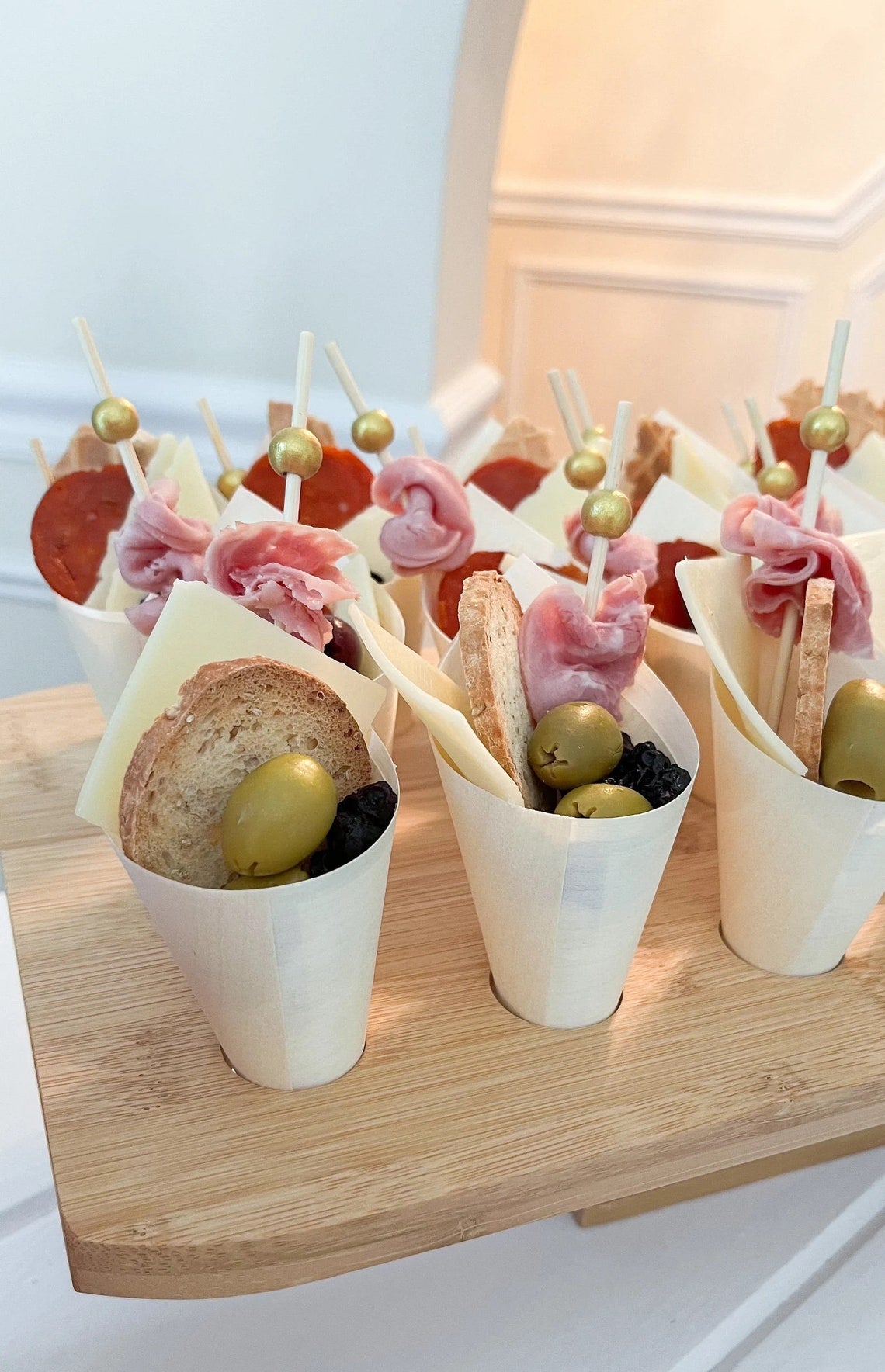 Disposable wooden charcuterie cones filled with meat, bread, and olives, presented on an eco-friendly bamboo stand.