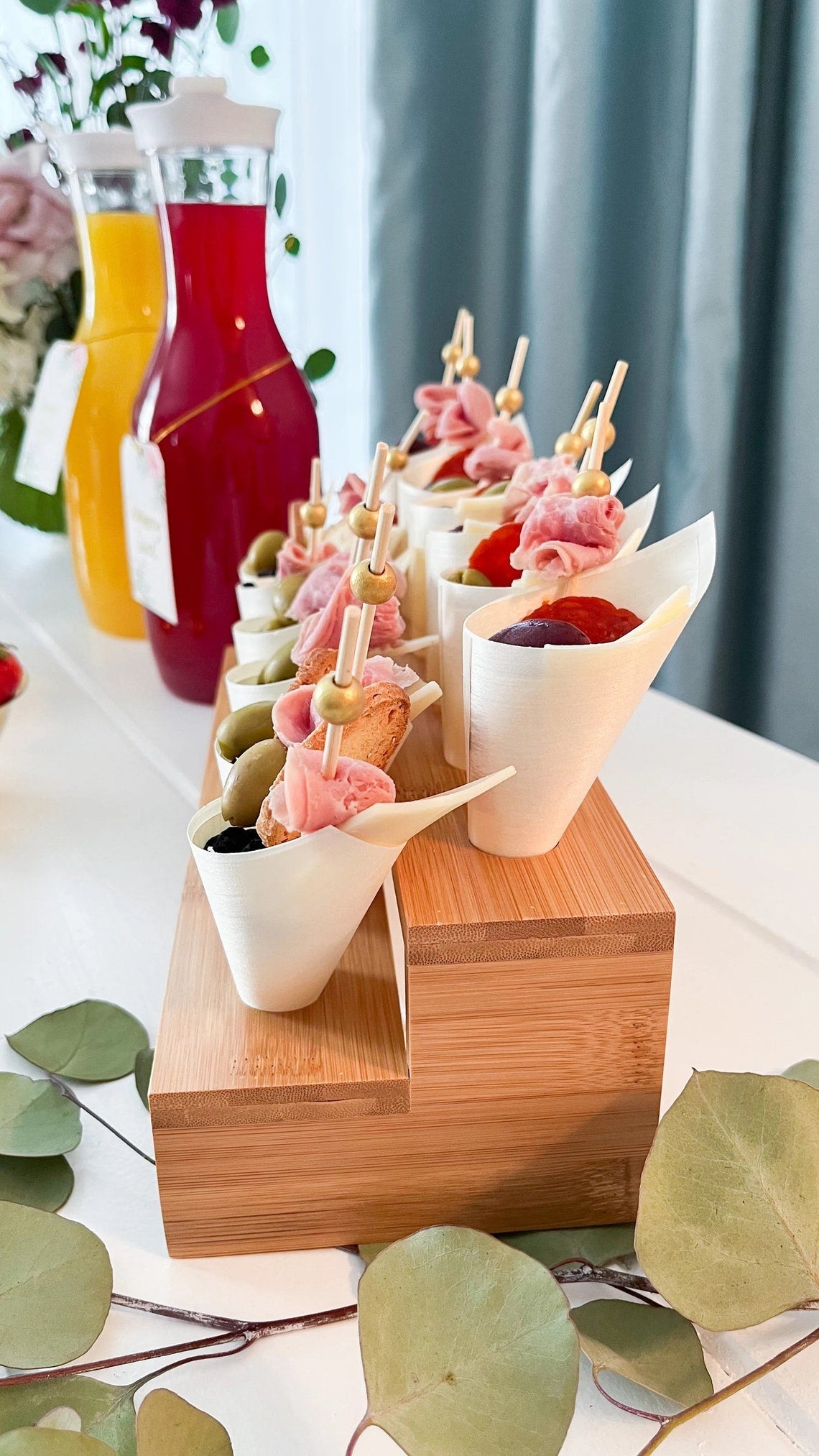 Charcuterie cups on a tiered wooden display stand. Disposable wooden cones for easy cocktail party appetizers.
