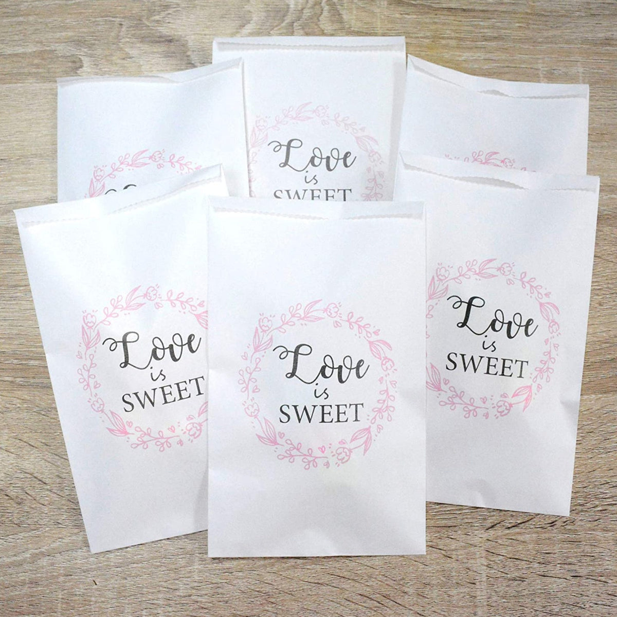 Multiple white paper party bags with pink floral wreath "Love is Sweet" design. Wedding candy favor bags.