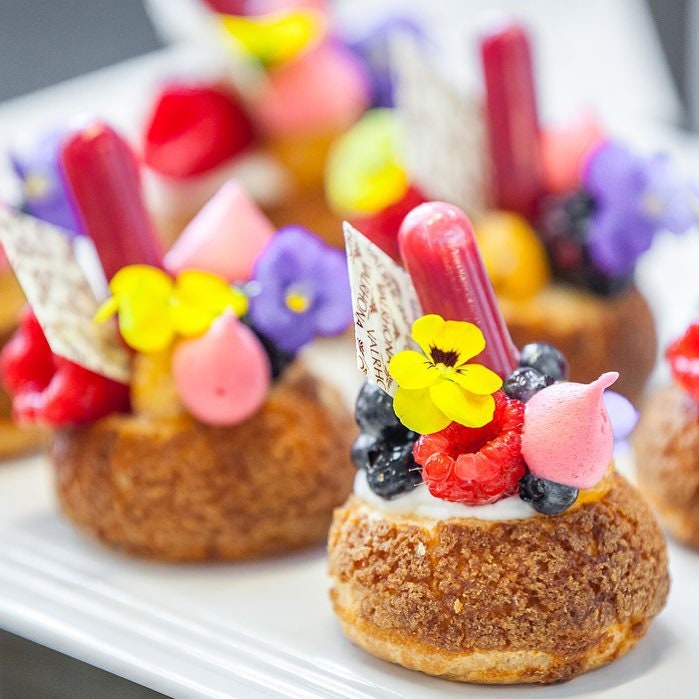 Decorative pastries with colorful toppings and a mini pipette on a white plate